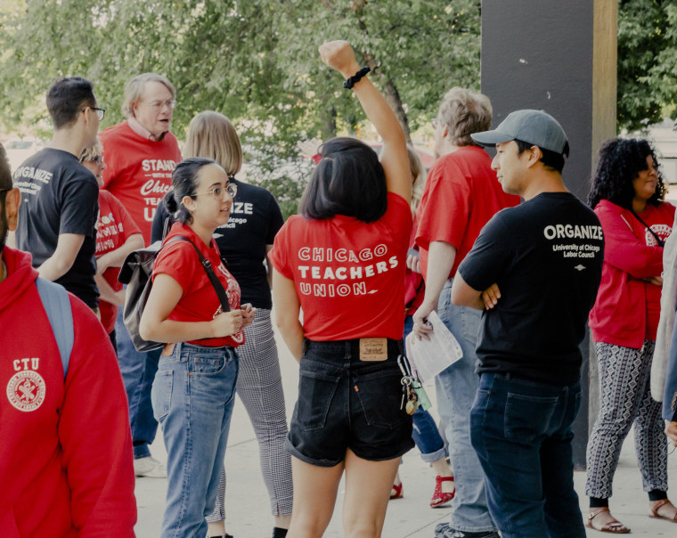 Image: A group of teachers and union representatives demonstrate outside the mayor's budget meeting at Roberto Clemente High school