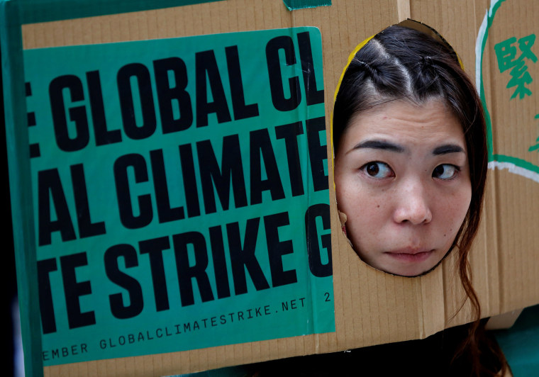 Image: A woman puts her face out of a banner at an event to mark the day of global climate strikes in Tokyo