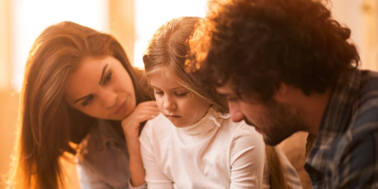 Image: Sad little girl at home being consoled by her parents.
