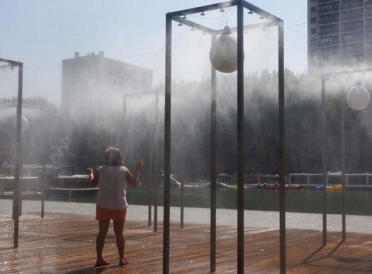 Image: A woman refreshes herself under water atomizers in Paris during a continent-wide heatwave in July.