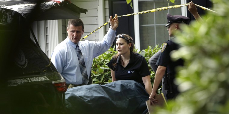 A woman from the Massachusetts Chief Medical Examiners Office, center, uses a gurney to place human remains into a vehicle as law enforcement officers hold caution tape at a home where two adults and three children were found dead with gunshot wounds, Monday, Oct. 7, 2019, in Abington, Mass