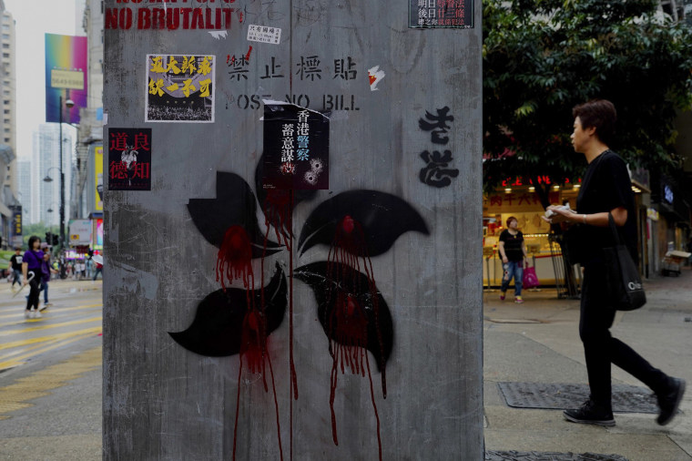 Image: People walk near graffiti on a pillar which shows Hong Kong Special Administrative Region flag pattern drawn in  black and red in Hong Kong