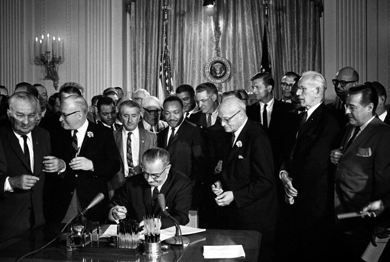 Image: President Lyndon B. Johnson signs the Civil Rights Act as Martin Luther King Jr. looks on at the White House in 1964.