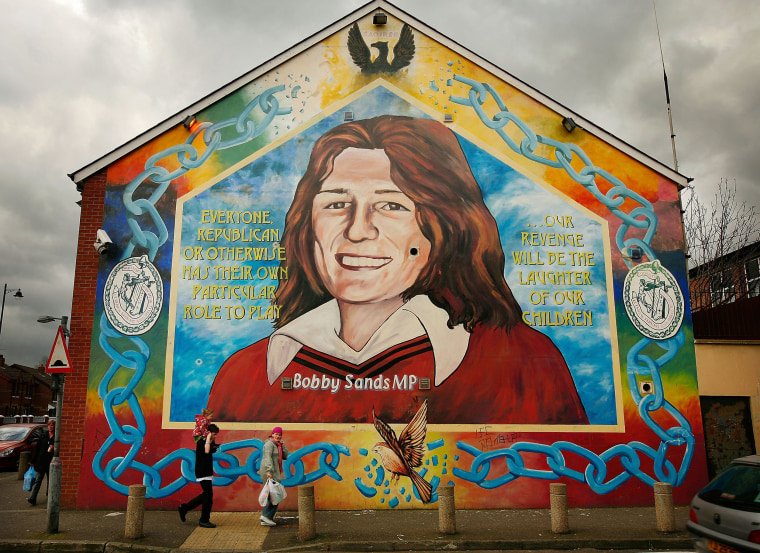 Image: A couple walks past a mural depicting Bobby Sands in the Falls Road on April 10, 2008, in Belfast.