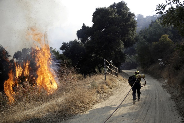 Image: A firefighter runs to hose down flames in Newhall, Calif., on Oct. 12, 2019.