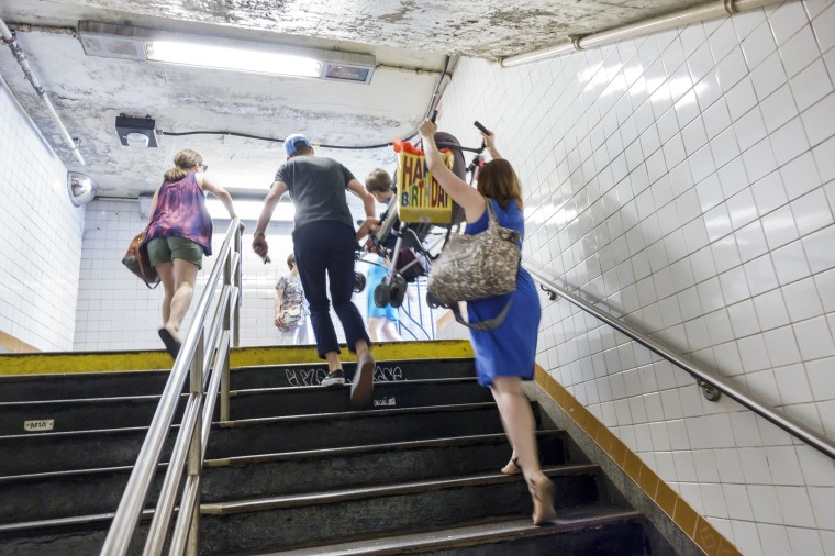 A man and woman carrying a stroller up the stairs in the Manhattan subway station.