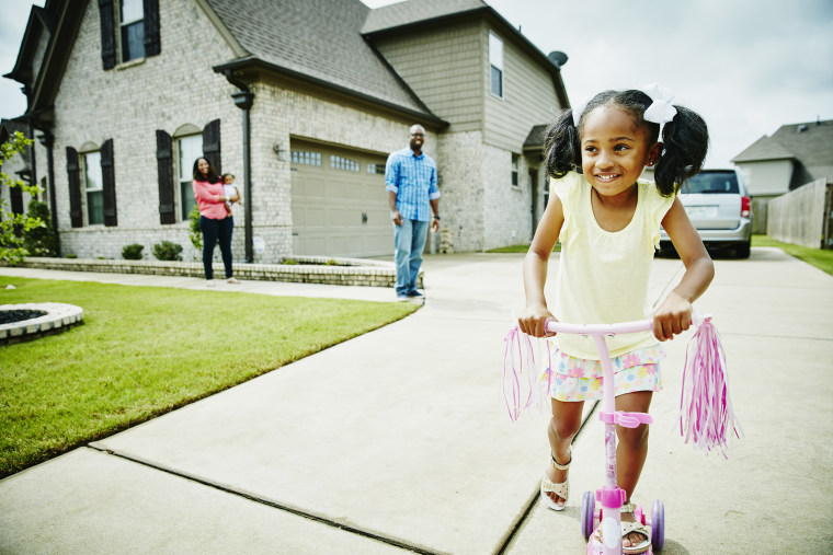 Image: Smiling young girl riding scooter in driveway