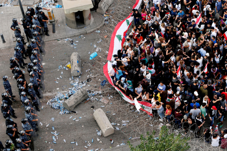 Image: Demonstrators carry flags as police stand behind barbed wire during protests in Beirut, Lebanon, on Oct. 19, 2019.