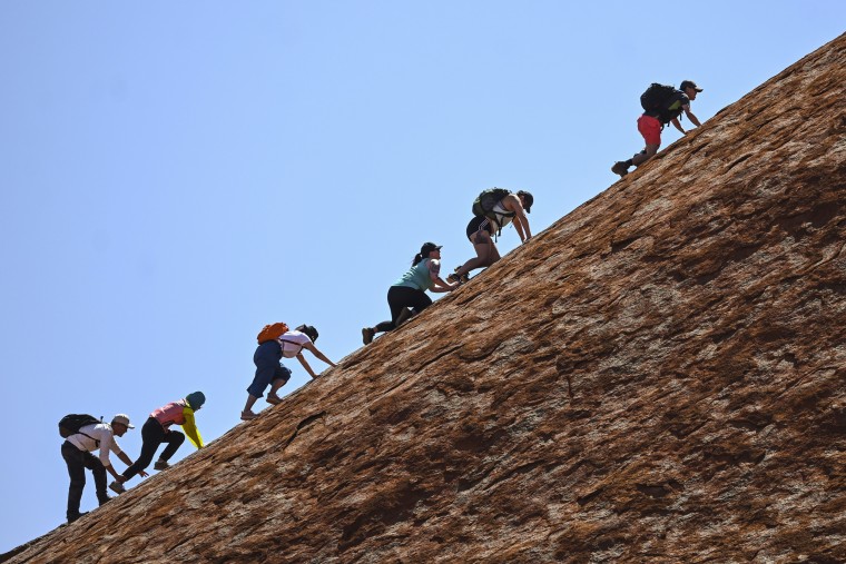 Image: Tourists climb Uluru.