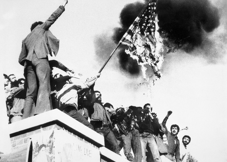 Image: Demonstrators perched atop of the U.S. Embassy wall burn an American flag