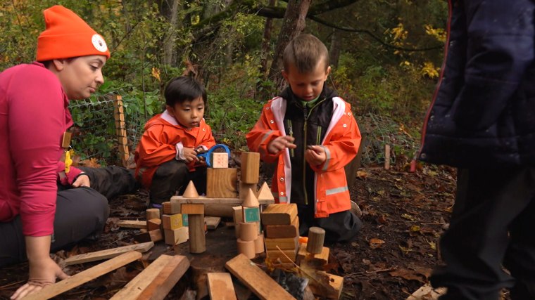 Two youngsters in Tiny Trees' outdoor preschool program play with building blocks on the ground.