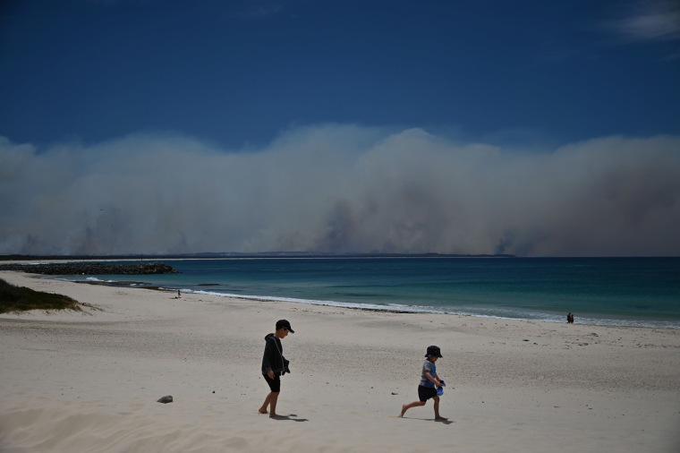 Image: Bushfires burn in the distance as children play on a beach in Forster, 300km north of Sydney on Nov. 9, 2019, as firefighters try to contain dozens of out-of-control blazes that are raging in the state of New South Wales.