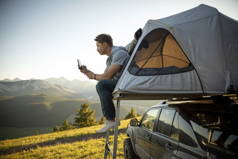 Serene man camping, relaxing at SUV rooftop tent in sunny, idyllic field, Alberta, Canada