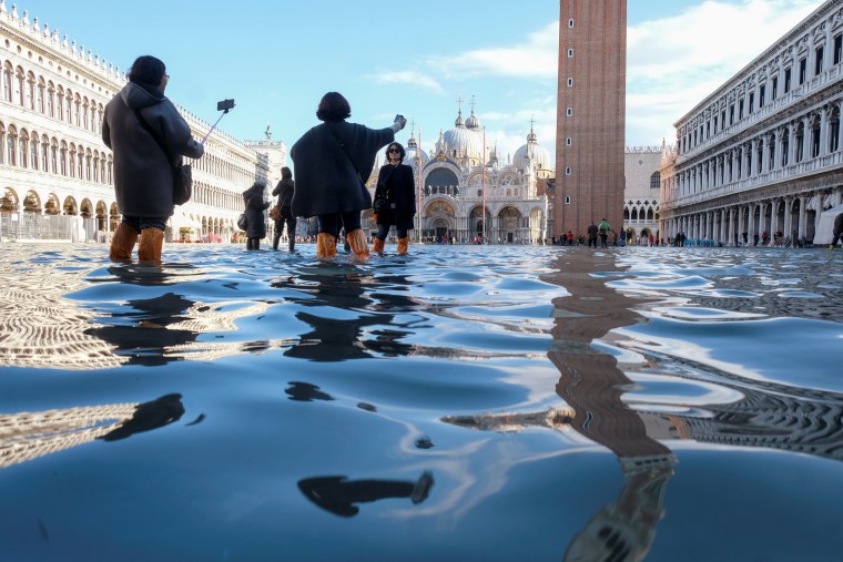 Image: Tourists take pictures in the flooded St. Mark's Square during a period of seasonal high water in Venice