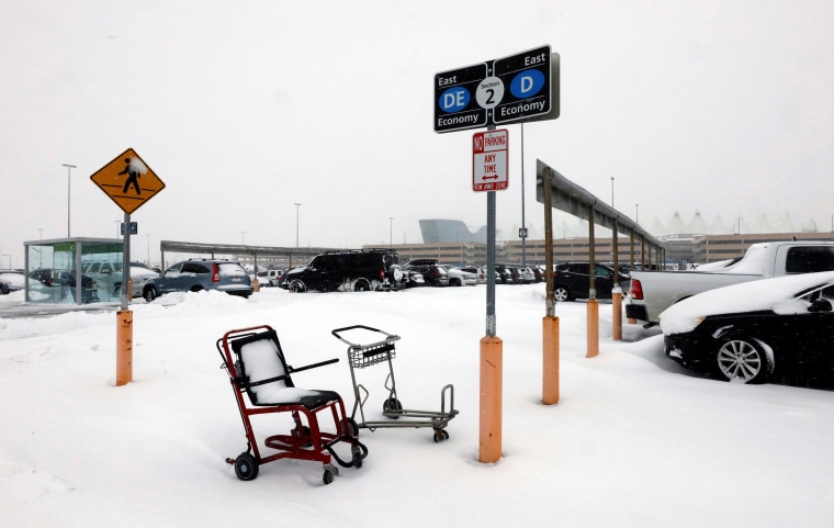Image: A wheelchair and luggage cart are covered in snow after a snowstorm at Denver International Airport