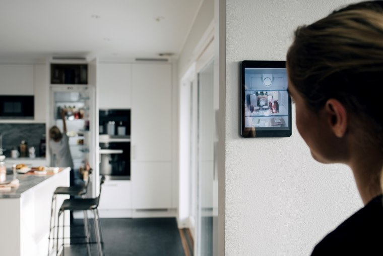 Rear view of teenage girl standing by wall with digital tablet looking at brother in kitchen