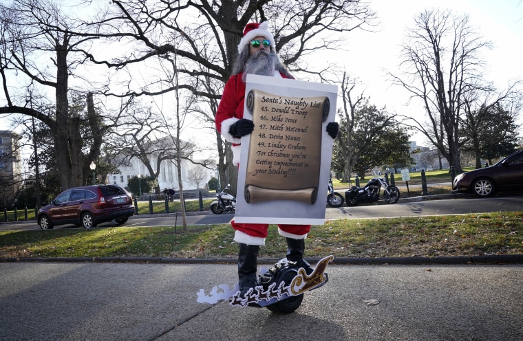 Image: A man dressed as Santa Claus holds a "naughty list" including members of the Trump administration near the Capitol on Dec. 18, 2019.