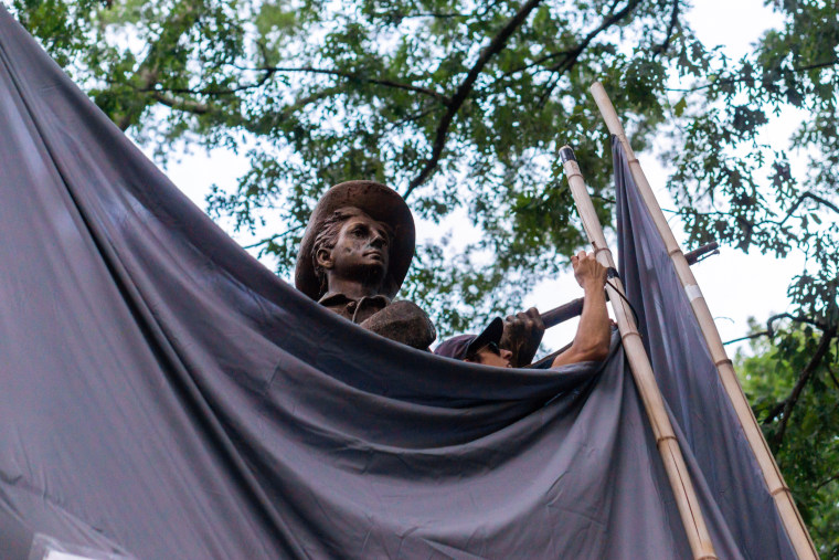A protestor zip-ties two bamboo poles together to obscure Silent Sam, a confederate monumnet on UNC-Chapel Hill's upper quad.
