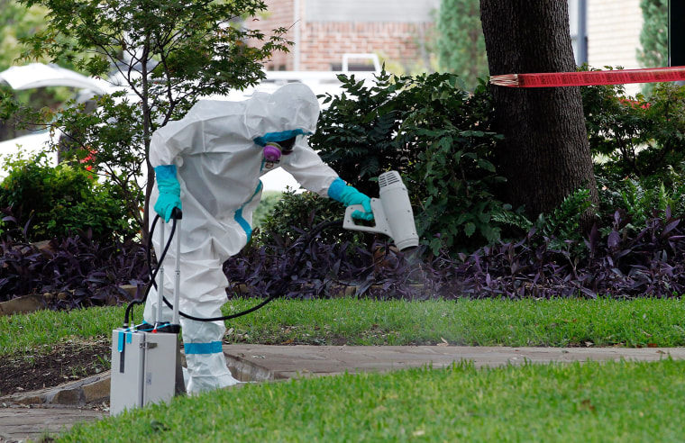Image: A man dressed in protective hazmat clothing treats the sidewalk in front of an apartment where nurse Nina Pham resides