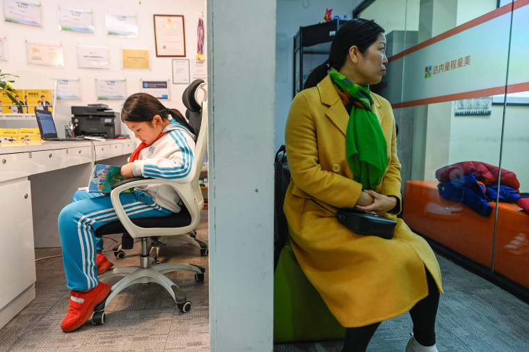 Image: A pupil reading a book outside a classroom as she waits to attend a class at a children's computer coding training centre in Beijing