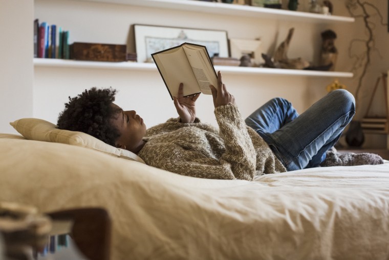 Young woman lying on bed reading a book