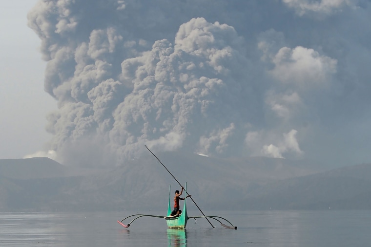 Image: A youth at the foot of Taal volcano rides an outrigger canoe while the volcano spews ash as seen from Tanauan town in Batangas province, south of Manila