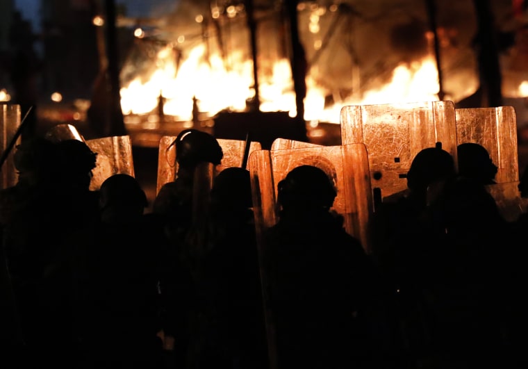 Riot policemen watch flames rise Saturday in Beirut from the tents of anti-government protesters, which where set on fire by civilian men believed to be the private unit of the parliament guards.