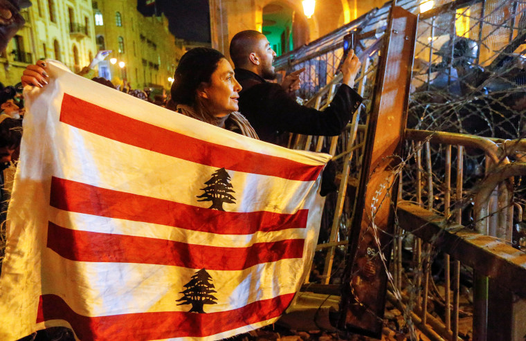 Image: A demonstrator holds the Lebanese flag during a protest against a ruling elite accused of steering Lebanon towards economic crisis in Beirut