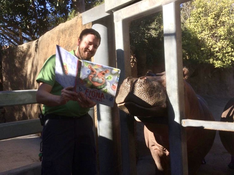 A caregiver at the San Antonio Zoo reads "A Very Fiona Christmas" to Timothy the Hippo.