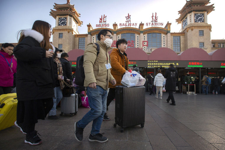 Image: A traveler wears a face mask as he walks outside Beijing Railway Station