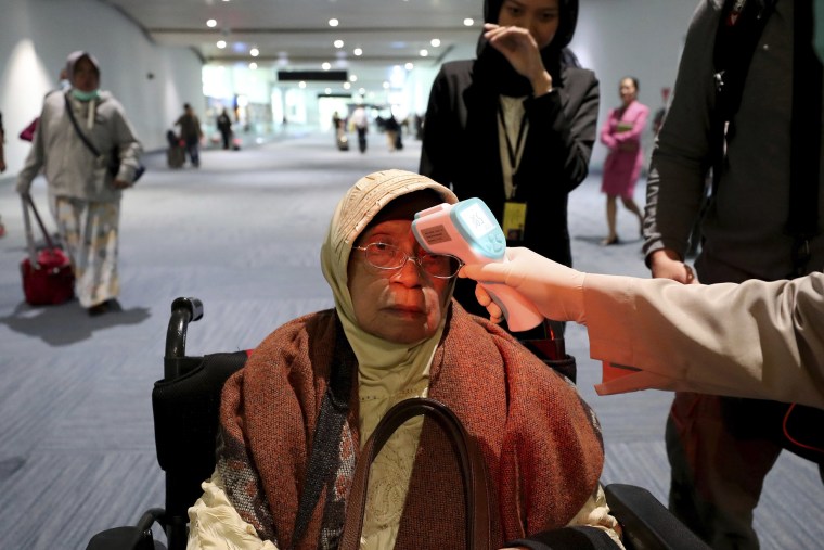 Image: A health official scans the body temperature of a passenger as she arrives at the Soekarno-Hatta International Airport in Tangerang, Indonesia