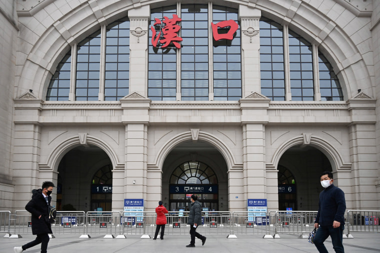 Image: People walk past the closed Hankou Railway Station after the city was locked down following the outbreak of a new coronavirus in Wuhan