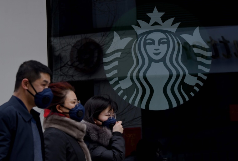Image: People wearing protective face masks walk past a closed Starbucks coffee shop at a grocery in Beijing