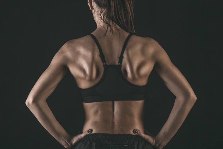 Rear view of female athlete wearing sports bra standing with hands on hip against black background