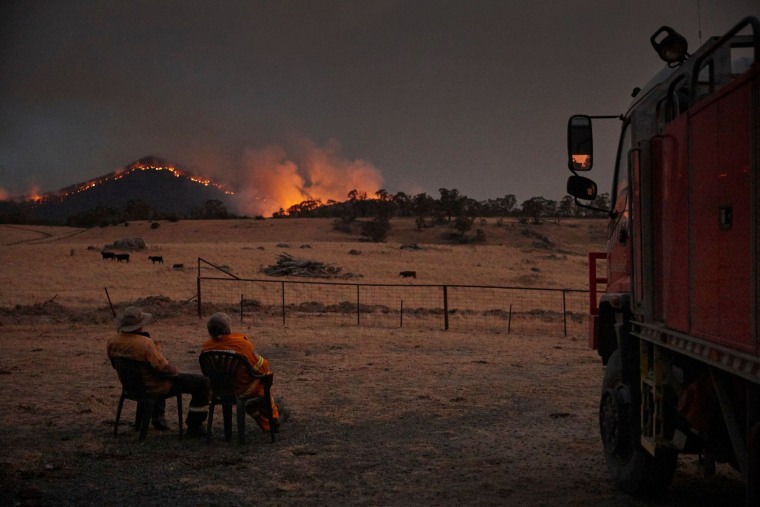 Image: Rural Fire Service volunteer firefighters watching as the New South Wales \"megafire\" approaches the outskirts of the town of Tumbarumba in New South Wales