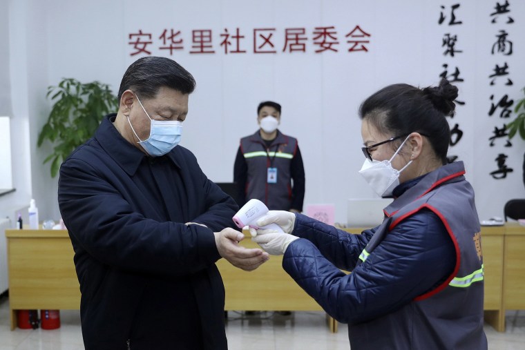 Image: Chinese President Xi Jinping, left, wearing a protective face mask, receives a temperature check as he visits a community health center in Beijing