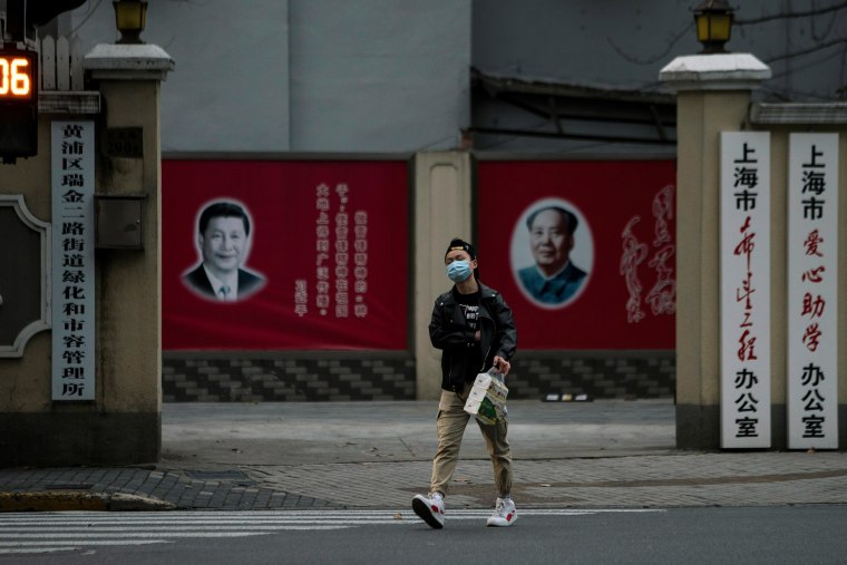 Image: A man wearing a mask walks by portraits of Chinese President Xi Jinping and late Chinese chairman Mao Zedong as the country is hit by an outbreak of the novel coronavirus, on a street in Shanghai