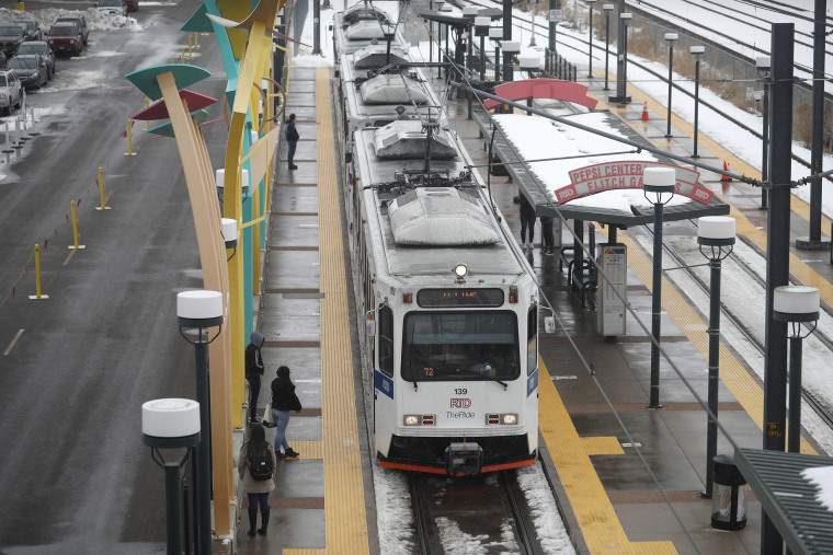 Image: Bundled up against cold temperatures and light snow, passengers wait for a light rail train to pull up to a station