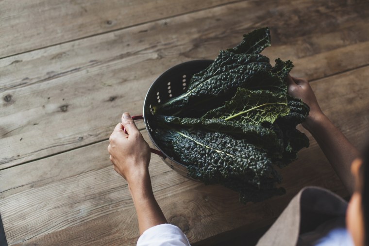 Cropped image of woman with kale in colander standing at wooden table