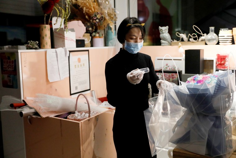 Image: A florist who prefers to be called Cai Xiaoman wearing a face mask and gloves, puts a bottle of hand sanitizer into a bouquet at a flowers shop in a shopping mall, as the country is hit by an outbreak of the new coronavirus, in Beijing