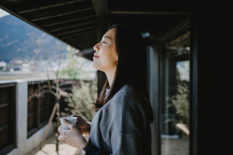 Beautiful young Asian woman drinking coffee and enjoying fresh air on balcony in the morning