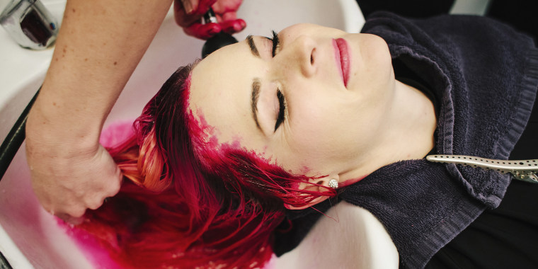 A hair salon client having red hair dye rinsed from her hair over a basin.
