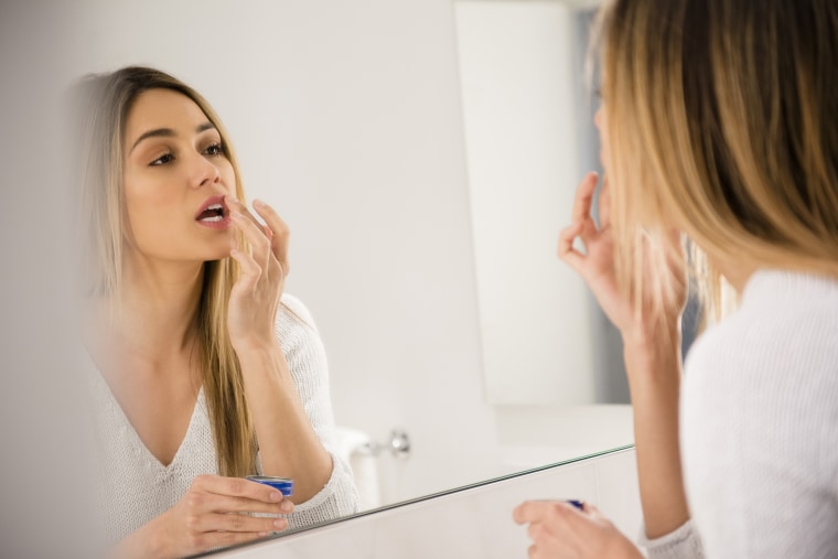 Image: Young woman looking in mirror and applying lip balm