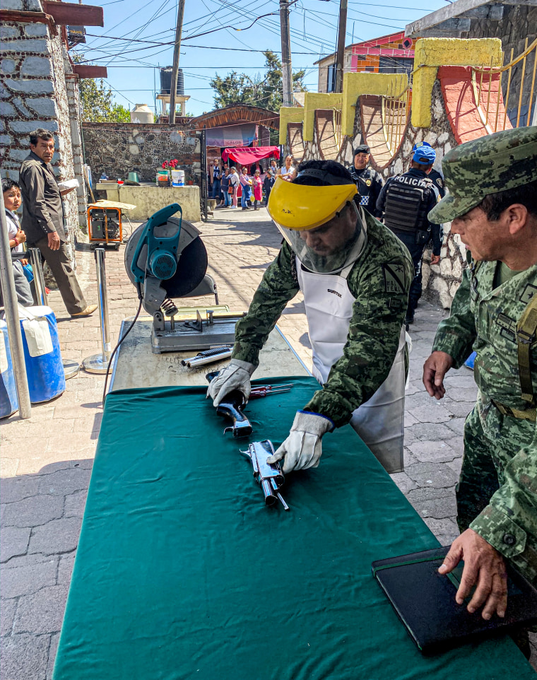 Image: A member of the military, protected by a face shield, cuts weapons turned in by citizens as part of a gun buyback program.