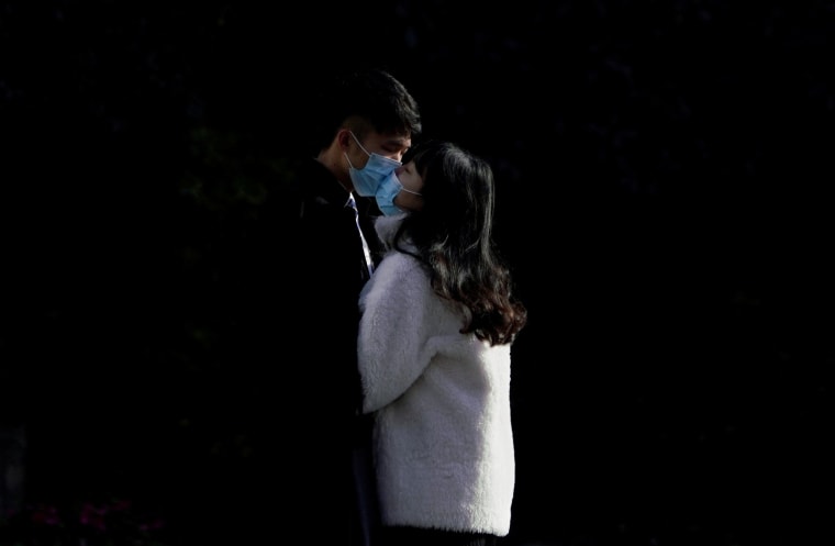 Image: A couple wearing masks kiss at a main shopping area, in downtown Shanghai