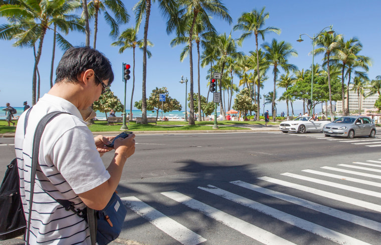 Image: A visitor texts before crossing the street in Waikiki on Oct,24, 2017 in Honolulu, Hawaii