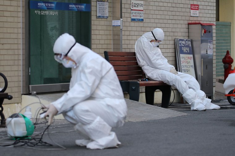 Image: A medical worker wearing protective gear takes a rest as he waits for ambulances carrying patients infected with the COVID-19 coronavirus at an entrance of a hospital in Daegu