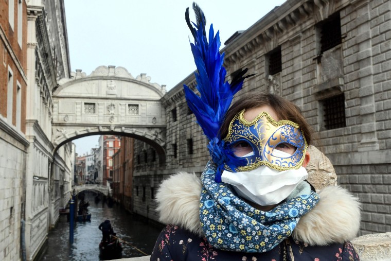 Image: A young tourist wearing a protective facemask and a Carnival mask visits the streets of Venice