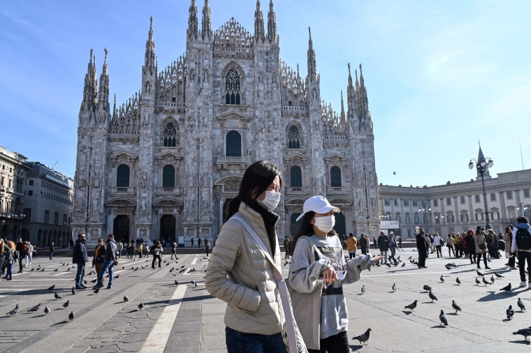 Two women wearing masks walk across the Piazza del Duomo in central Milan, on Feb. 24, 2020.
