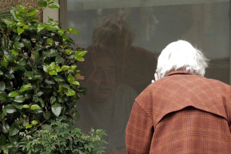Image: Campbell waves while talking through a window to her husband at a long-term care facility linked to several confirmed coronavirus cases in the state in Kirkland